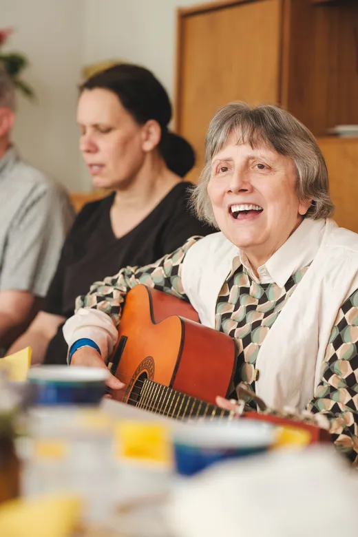 Eine Frau spielt Gitarre und singt, daneben sitzt eine weitere Person