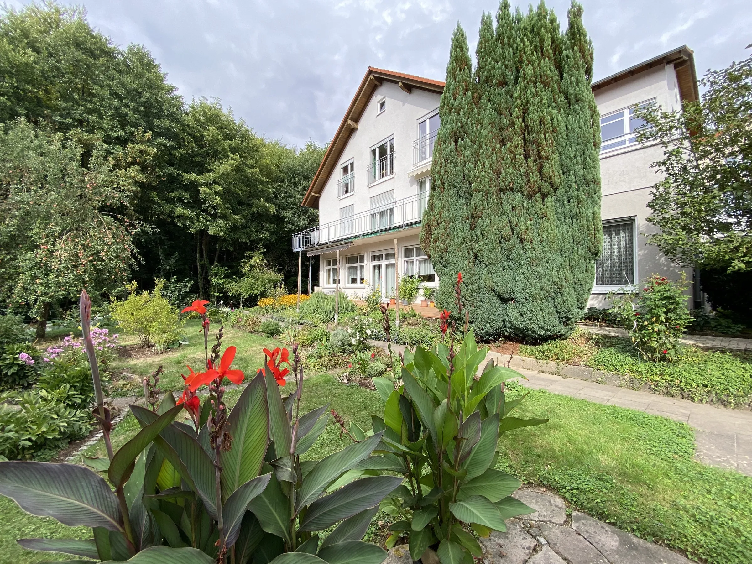 Das Missionsheim hinter dem Garten, im Vordergrund blühende Canna
