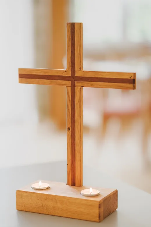 Ein Holzkreuz auf einem Sockel, davor zwei Teelichter