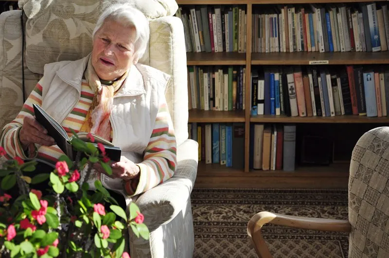 Eine Frau liest in einem Sessel vor einem Bücherregal