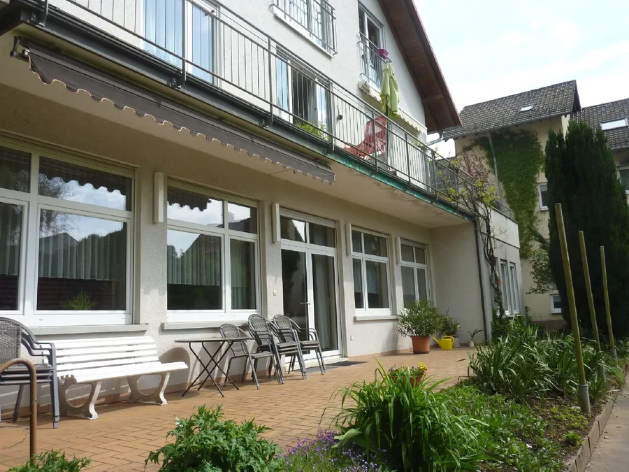 Terrasse mit Bank, Tisch und Stühlen vor einer Fensterfront